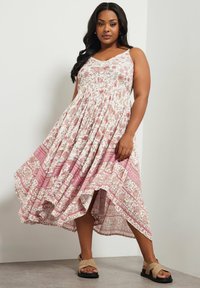 Vestido de estampado floral con escote en V, tirantes finos y un dobladillo asimétrico. La tela es ligera con patrones en rosa y blanco.
