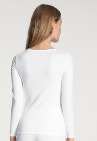 Witte lange mouwen top gemaakt van rekbaar materiaal. Heeft een ronde halslijn en een aansluitend ontwerp, met een gladde textuur en zonder zichtbare patronen.