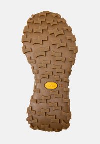 Brun gummisula med upphöjt strukturerat mönster och gul Vibram-logotyp, storlek 38 märkt nära mitten.