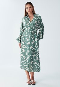 Duga, zelena haljina s uzorkom od lagane tkanine, s prednjim kopčanjem na gumbe, ovratnikom i pojasom vezanim u mašnu na struku.