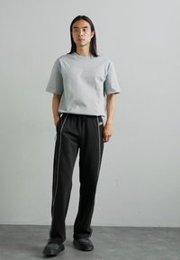 T-shirt gris clair à manches courtes associé à un pantalon de survêtement noir avec des bandes blanches sur le côté, une taille élastique et une coupe ample. Chaussures noires.