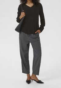 Schwarzes Langarmoberteil mit V-Ausschnitt, graue plissierte Hose und schwarze Absatzmule mit Schleifendetail. Strukturierter Stoff in lässiger Passform.