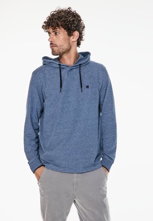 Felpa blu melangiata con cordino regolabile, tasca frontale e logo brandizzato. Abbinata a pantaloni grigi chiari, con una vestibilità comoda.