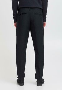 Schwarze maßgeschneiderte Hose mit geradem Schnitt, ausgestattet mit zwei Gesäßtaschen und einer glatten Stoffoberfläche, getragen mit schwarzem Schuhwerk.