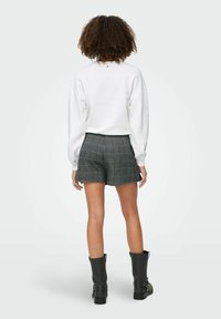 Bijela dukserica s niskim ramenima, karirane sive kratke hlače i crne čizme do gležnja s kopčama. Tkanina ima teksturirani završetak.