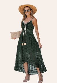 Groene maxi-jurk van kant met een high-low zoom, bloemmotieven, verstelbare bandjes en een gevlochten tailleband. Gecombineerd met een strohoed en accessoires.