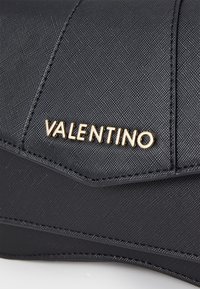 Black textured fabric purse with gold "Valentino" logo, featuring angular design and contrasting edges. Compact and sleek appearance.