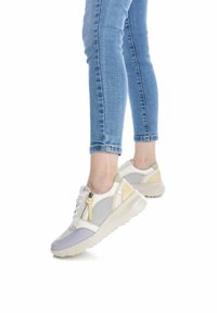 Zapatillas con una parte superior de malla transpirable, acentos en crema, amarillo claro y gris, con un zipper lateral y una suela blanca gruesa.