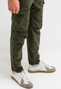 Olijfgroene cargo pants met elastische tailleband en zijzakken, gecombineerd met wit en grijs sneakers met een gumrubberen zool.