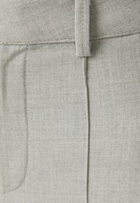 Szara tkanina o teksturowanym splocie, z pionowym szwem i delikatnym zarysem kieszeni. Pas posiada centralny haft.