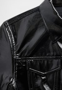 Juoda, blizgi dirbtinės odos marškinėliai su smailia apykakle, kontrastiniu siuvimu ir krūtinės kišene. Lygus paviršius su blizgiu apdaila.