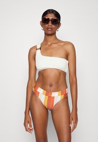 Top de bikini branco canelado de um ombro só com detalhes em metal; parte de baixo de cintura alta listrada em multicolorido nas cores laranja, amarelo e branco.