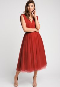 Czerwona sukienka midi z tiulu z dekoltem w kształcie litery V, rękawami typu cap oraz dopasowaną talią. Spódnica jest warstwowa, co tworzy zwiewną sylwetkę.