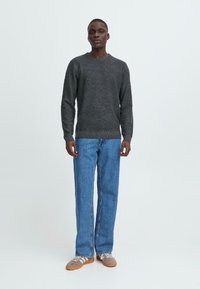 Grå strikket genser med rund hals, sammen med blå rette jeans. Brune sneakers med hvite lisser fullfører antrekket.