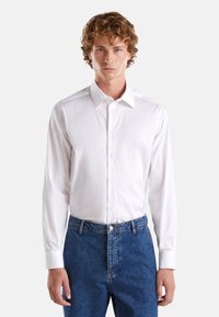 Camicia bianca a maniche lunghe con colletto classico e tessuto morbido, abbinata a pantaloni in denim blu con vita standard e cinque tasche.