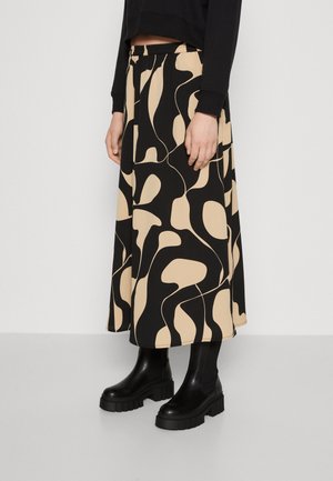 Kvinde iført en beige og sort midi-nederdel med abstrakt mønster, kombineret med sorte chunky platform ankelstøvler og en sort cropped sweatshirt.