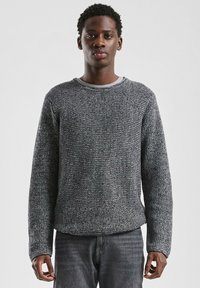 Grijze gebreide trui met een gestructureerd patroon, ronde halslijn en lange mouwen, gecombineerd met donkere denim jeans.