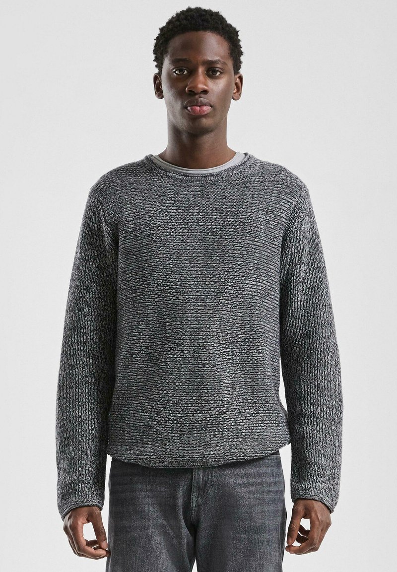 Grijze gebreide trui met een gestructureerd patroon, ronde halslijn en lange mouwen, gecombineerd met donkere denim jeans.