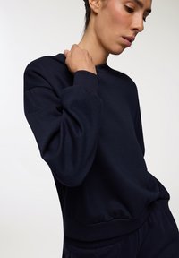 Granatowy sweatshirt z okrągłym dekoltem, ściągaczami przy mankietach i w pasie. Wykonany z teksturowanej tkaniny, z luźnym krojem.