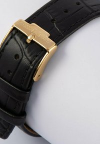 Schwarzes Lederarmband mit strukturiertem Muster, ausgestattet mit einer goldenen Metallschließe, die mit "Jacques Lemans" graviert ist.