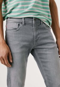 Jeans de mezclilla gris claro con corte recto, que cuentan con bolsillos frontales, costuras sutiles y una pequeña etiqueta con una bandera en el bolsillo.