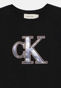 Black cotton t-shirt featuring a large "ck" logo in a glossy, cloud-patterned design outlined in light beige. Round neck.
