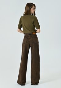 Pantalons amples marron avec des ourlets effilochés, associés à un haut ajusté vert olive à manches courtes. Le matériau semble lisse et extensible.