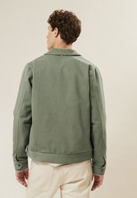 Groene katoenen jas met een geknoopte kraag, zichtbare stiksels en een cropped ontwerp. Heeft lange mouwen en een gladde, textuurlijke afwerking.