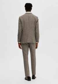 Costume à carreaux gris avec une veste à un bouton, des revers crantés et un pantalon droit. Complété par des chaussures de ville noires.