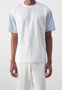 Valkoinen puuvillapaita, jossa on raidalliset siniset lyhyet hihat, pyöreä pääntie ja rento malli. Sujuva pinta ja minimalistinen muotoilu.