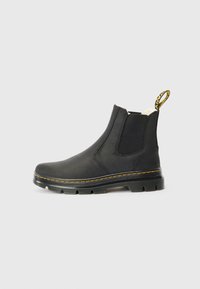 Bota Chelsea preta de couro com sola de borracha espessa, costura amarela, painéis laterais elásticos e uma alça com texto amarelo.
