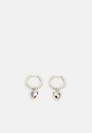 Sølv øreringe med små skinnende hjerteformede charms, der hænger indeni hver ring på en hvid baggrund.