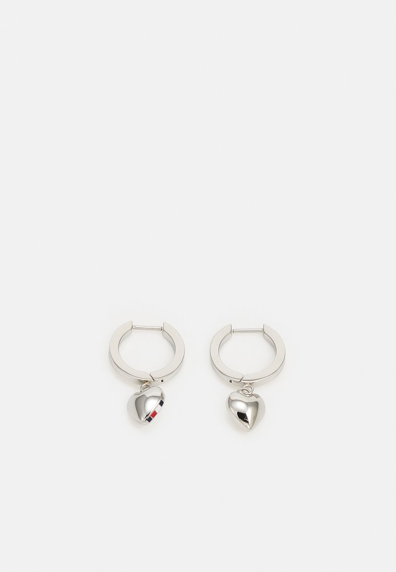 Boucles d’oreilles anneaux en argent avec de petits charms brillants en forme de cœur suspendus à l’intérieur de chaque anneau sur fond blanc.