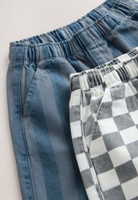 Dve pari kratkih hlač: ene so modre z navpičnimi črtami, druge bele s črno karo vzorcem; obe imata elastične pasove.