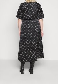 Schwarzes Kleid mit weißen Punkten, kurzen Ärmeln, lockerer Passform und mittellangem Rock. Glatter Stoff und Rückenpasse. Getragen mit schwarzen Stiefeln, die bis zum Knie reichen.