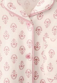 Ljusrosa pyjamasöverdel med blommönster, med korta ärmar, en krage, en ficka och rosa knappar framtill.