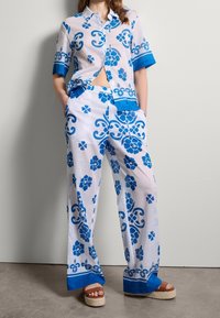 Ensemble en tissu léger et transparent avec un motif floral bleu sur fond blanc. Chemise à manches courtes et pantalon large avec des accents bleus.
