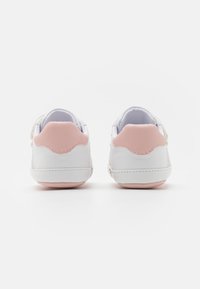 Białe sneakersy z różowymi akcentami, charakteryzujące się gładką skórzaną powierzchnią, zaokrąglonym kształtem i teksturowanymi detalami na pięcie dla lepszej przyczepności.