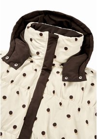 Prešívaná bunda v krémovej farbe s hnedými bodkami, má vysoký golier, zapínanie na zips a patentové gombíky na légach pre zvýšenú funkčnosť.