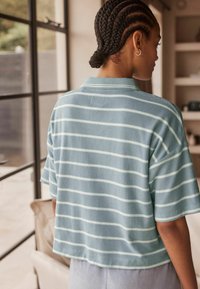 Himmelblaues Poloshirt mit kurzen Ärmeln und weißen horizontalen Streifen. Hergestellt aus weichem Stoff, mit einem Kragen und lässiger Passform.