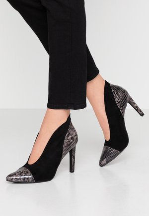 Schwarze High Heels mit spitzen Zehen und Schlangenprint-Akzenten an Fersen, Zehen und dem hinteren Bereich, getragen zu schwarzen Culottes.