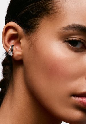 Primer plano del oído de una persona que lleva un pendiente de aro plateado con un pequeño colgante en forma de flor.