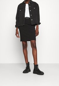 Černá džínová bunda s třepeným lemem, bílé tričko s kulatým výstřihem a logem, černá tužková sukně a masivní černé kotníkové boty. Hladké textury.