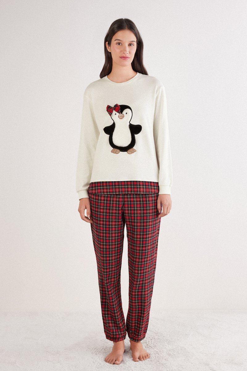 Sudadera blanca de manga larga con un aplique de pingüino; pantalones de pijama de cuadros rojos y negros con puños elásticos.