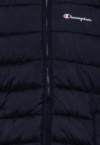 Gilet imbottito di colore blu navy con motivo trapuntato verticale, zip frontale completa e logo Champion ricamato in bianco sulla parte superiore sinistra del petto.