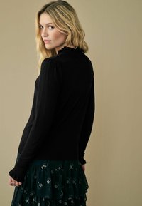 Maglione nero con scollo arricciato e maniche lunghe, abbinato a una gonna arricciata con motivo floreale verde. Texture liscia.