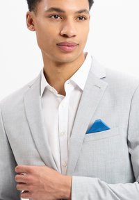 Lichtgrijze blazer met een subtiele textuurpatroon, witte shirt eronder en een blauwe pochet als accent. Getailleerd ontwerp met notch-lapels.