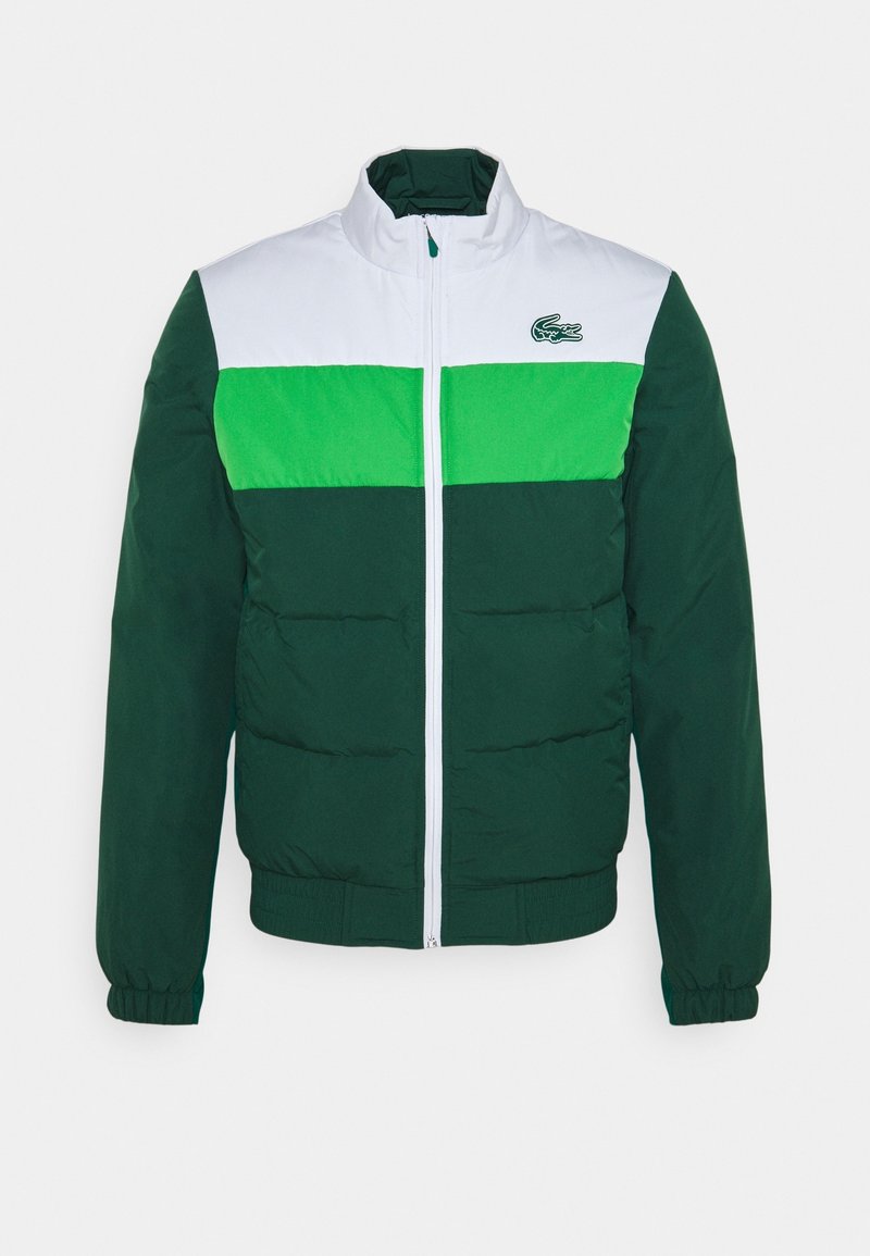 Färgat blockjacka med vit överkropp, ljusgrön rand och mörkgrön underdel och ärmar, med en liten krokodil-logotyp på bröstet.