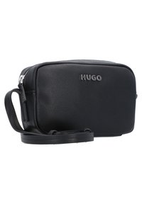 Black leather crossbody bag with a textured surface, silver logo, zip closure, and an adjustable strap. Compact rectangular shape.