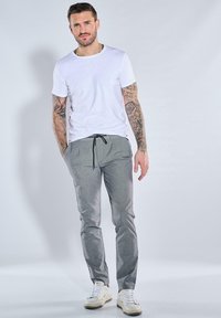 Weißes T-Shirt mit kurzen Ärmeln und graue Sweatpants mit Kordelzug. Die Hose hat eine glatte Textur, während die Schuhe weiß mit beigen Akzenten sind.